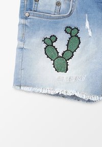 Pantalones cortos de mezclilla en azul claro con dobladillo deshilachado. Presentan un cactus bordado en verde y el texto "SOY PINTOR" en costura blanca.