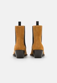 Bruna mocka ankelskor med svarta elastiska sidopaneler och en liten, staplad klack. Har en ögla baktill för lätt påtagning.