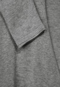 Grått stickat tyg med en mjuk textur. Har en vikt manschett och en jämn yta som visar subtila variationer i trådfärgen.