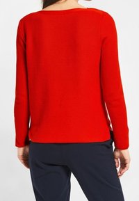 Roter Strickpullover mit Rundhalsausschnitt, langen Ärmeln und strukturiertem Finish, kombiniert mit dunklen Hosen, von hinten gesehen.