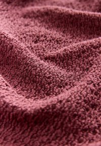 Tissu texturé d'une couleur bordeaux profond, présentant une surface froissée avec des motifs en relief, créant une apparence douce et chaleureuse.