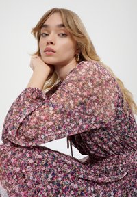 Bloemeneen jurk van een roze, doorzichtige stof met meerkleurige bloemen. Lange pofmouwen, elastische manchetten en een getailleerd taille detail.