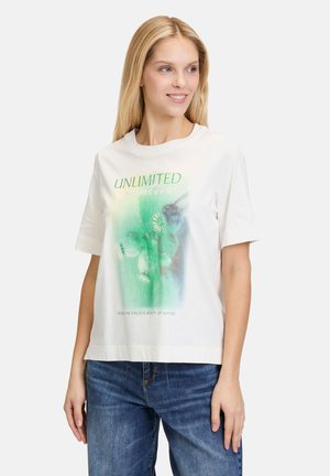 Hvid bomulds t-shirt med en afslappet pasform, der har et grønt grafisk print og tekst, der siger "UNLIMITED," sat sammen med blå denim jeans.