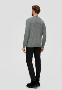 Grauer Strickpullover mit langen Ärmeln, Rundhalsausschnitt, mit einer strukturierten Oberfläche, kombiniert mit schwarzen schmalen Hosen und schwarzen Schnürstiefeln.