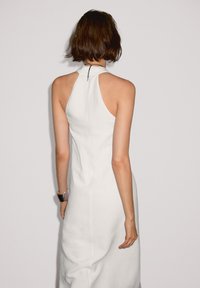 Weißes Neckholderkleid mit taillierter Silhouette, glatter Textur und Reißverschluss auf der Rückseite. Der Stoff wirkt leicht und strukturiert.