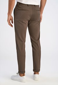 Bruine op maat gemaakte broek van zachte stof, met een slim fit, opgerolde mouwen en twee achterzakken. Gecombineerd met witte sneakers.