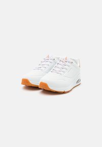 Chaussures de sport blanches avec semelle en caoutchouc orange, tige en maille et synthétique, bout rond et fermeture à lacets. Côtés texturés et détails de marque visibles.