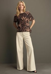 T-shirt noire avec un motif de feuilles de pêches, à manches courtes, associé à un pantalon beige à jambes larges. Texture lisse, coupe décontractée et design sobre.