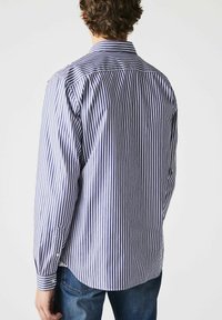 Striped button-up shirt featuring blue and white vertical stripes, long sleeves, a collar, and rounded hem, made from a smooth fabric.