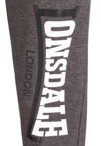 Pantalones deportivos grises con letras grandes en blanco que dicen "ONSDALE" y "LONDRES" en el costado, fabricados con una suave tela texturizada.
