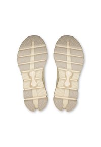 Suelas de zapatillas de correr beige con goma texturizada y ranuras flexibles, que presentan un elemento de amortiguación central y patrones de banda de rodadura variados.