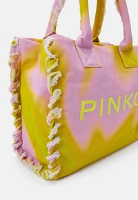 Kangaskassi, jossa on vaaleanpunainen ja keltainen sitruunakuviot, fringed-reunat ja sana "PINKO" brodeerattuna keltaisella. Vankat kahvat.