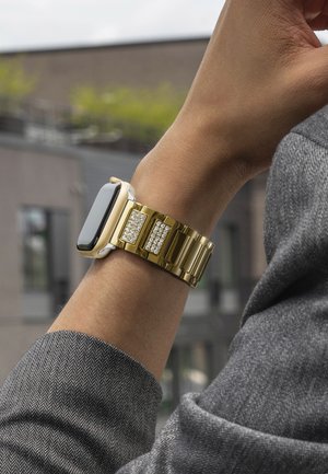 Montre en métal doré avec un écran noir brillant, mettant en avant des accents scintillants sur le bracelet. Le bracelet a une finition brillante et maillée.