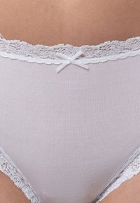 Mutande alte bianche con pizzo e un piccolo fiocco in vita su un addome inferiore.