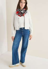 Jasnoszara krótka kardiganka nałożona na białą sweter ribbed, w połączeniu z szerokimi niebieskimi dżinsami. Szalik ma czarno-czerwono-białą geometrię wzoru.