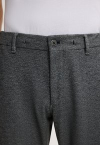 Graue Hosen mit Kieselsteinmuster, ausgestattet mit einem Knopfverschluss und Gürtelschlaufen. Der Stoff wirkt strukturiert und strapazierfähig, geeignet für lässige oder formelle Anlässe.