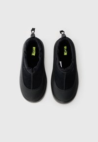 Pair of black slip-on UGG shoes with textured rubber soles and adjustable pull tabs, shown from above on a white background.