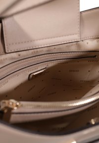 Interno della borsa color beige chiaro, caratterizzato da finta pelle liscia, scomparti con zip e una fodera a motivo logo in tonalità discrete.