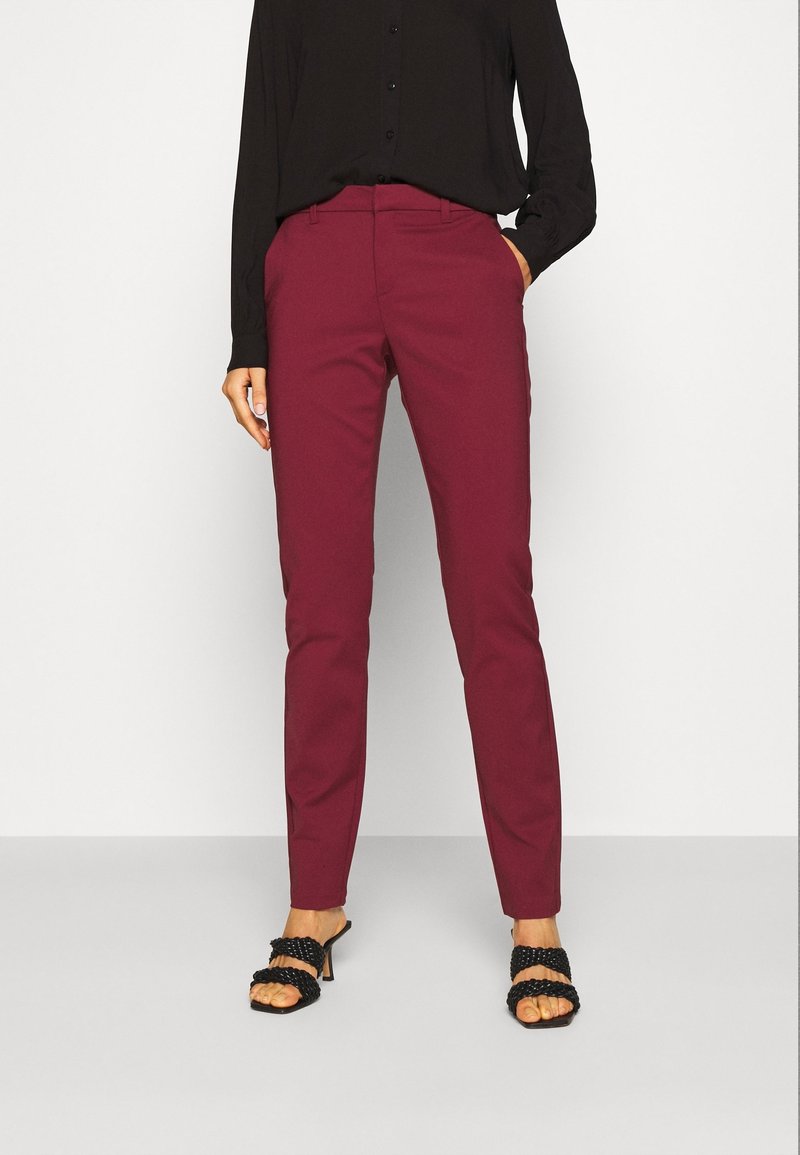 Pantalons ajustés bordeaux en tissu lisse avec une coupe slim, associés à des sandales à talons noires avec des bretelles tressées.