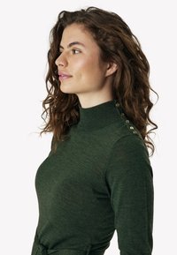 Sötétzöld kötött pulóver magas gallérral, arany gombokkal a válltömésen és formás szabással.