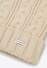 Béžová pletená čepice se vzorem copánku, s žebrovaným lemem a stříbrnou etiketu s nápisem "WITTCHEN". Měkká textura s hustou přízí.