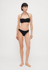 Black bikini with a textured design, featuring a bandeau top and adjustable halter straps. The bottom has a low-rise cut.
