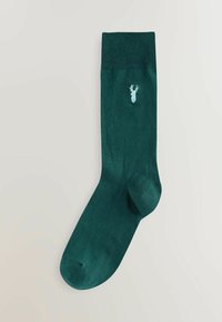 Mørkegrøn sok med ribbet manchet, der har et lille, lyseblåt hjorteemblem. Fremstillet af blødt, struktureret materiale for maksimal komfort.
