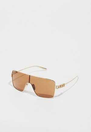 Ochelari de soare cu ramă aurie, cu lentile mari dreptunghiulare de culoare maro și logo-ul decorativ "GUESS" din strass pe brățările subțiri.