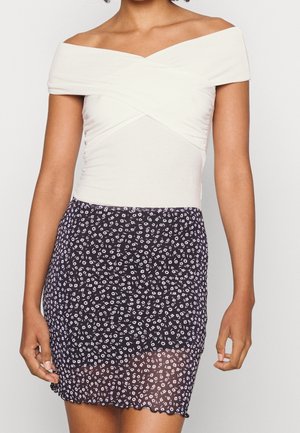 Vrouw draagt een wit off-shoulder top gecombineerd met een zwarte minirok met een klein wit bloemenpatroon.