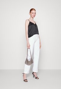 Top in satin nero con pizzo, abbinato a pantaloni bianchi a gamba larga e sandali con tacco neri. Modella che tiene una borsa a tracolla metallica argento.