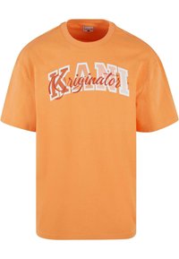 Orange bomulds T-shirt med korte ærmer. Har fed hvid tekst "KANI" og kursiv "Kriginator" med kontrasterende røde accenter. Lige pasform.