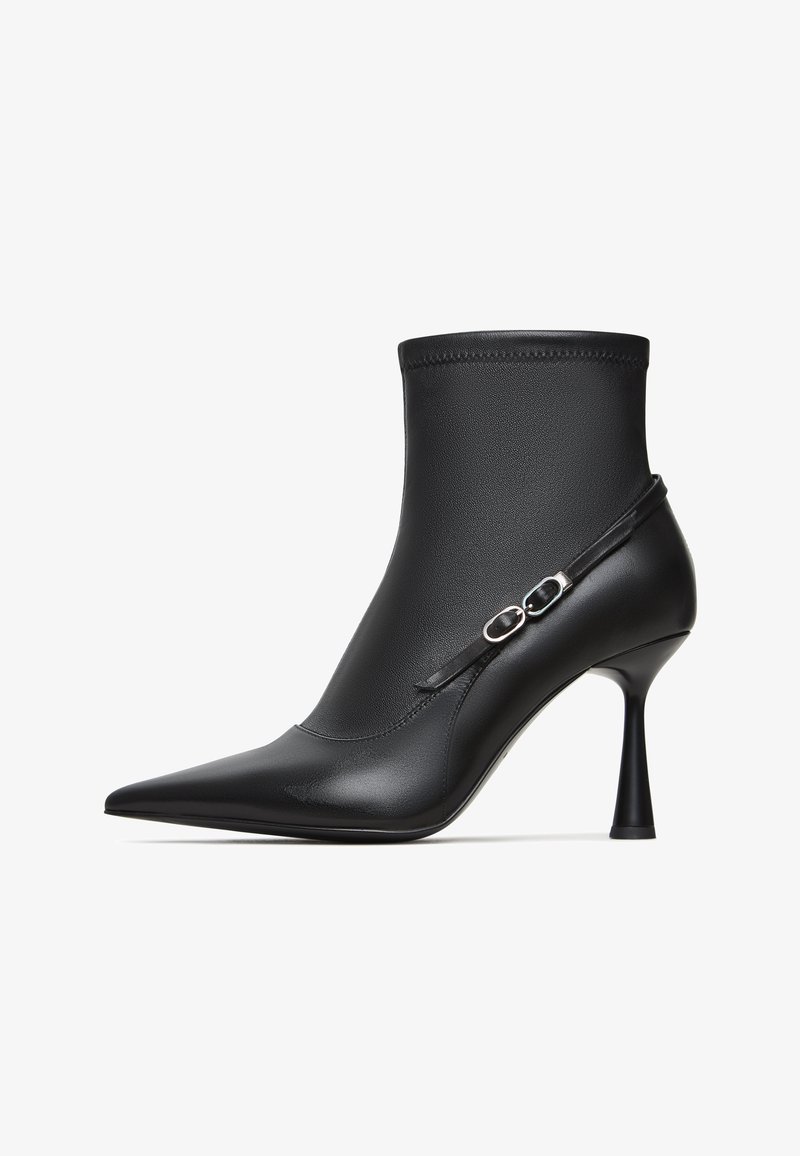 Fekete, hegyes orrú bokacsizma sima bőrből, szorosan illeszkedő szára és vékony stiletto sarka van díszítő pánttal.