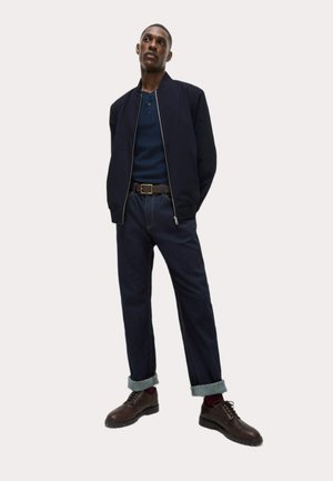 Chaqueta de piloto navy sobre una camiseta henley azul, jeans de mezclilla oscuros con los puños remangados, botas marrones con cordones y un cinturón marrón. Diseño sencillo y moderno.