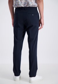 Marineblaues Hosen aus gewebtem Stoff mit zwei hinteren Taschen mit Knöpfen, schmal zulaufendem Bein und leichtem Glanz, kombiniert mit weißen Sneakern.
