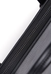 Sort lædertaske med en tekstureret overflade og en sølvfarvet lynlås. Lynlåse tænder er synlige, hvilket giver en detaljeret kant langs åbningen.