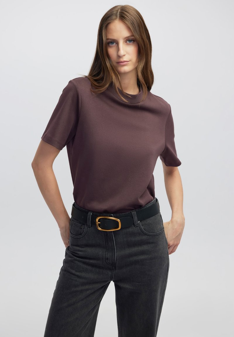 Camiseta de manga corta color morera hecha de una tela suave, combinada con jeans oscuros de tiro alto y un cinturón negro con una hebilla dorada.