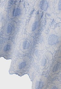 Tissu à motifs floraux dans des nuances de bleu et de blanc avec une surface texturée. Présente de grands designs de fleurs avec des bords festonnés.