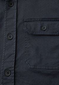 Dunkelgrauer Hemdenstoff mit schwarzen Knöpfen, auf denen "STREET ONE" geprägt ist, und einer mit Knöpfen verschlossenen Klappentasche auf der rechten Seite.