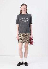 Graues T-Shirt mit dem Aufdruck "RAGING CLUB FROM FUTURE", kombiniert mit einem Minirock im Leopardenmuster. Die Accessoires umfassen eine kleine rote Handtasche.