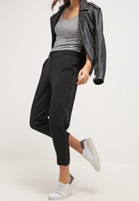 Schwarze, taillierte Hosen mit hoher Taille, kombiniert mit einem gestreiften Tanktop und einer schwarzen Lederjacke. Weiße Sneaker mit grauen Akzenten.