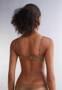 Brun behå med justerbara remmar, hak-och-öga stängning, slät tyg och en sömlös baksidedesign. Minimalistisk estetik utan mönster.