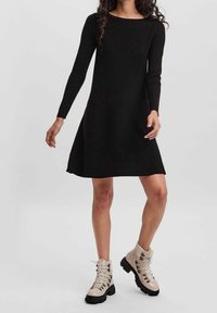 Robe noire à manches longues avec une coupe décontractée, réalisée en tissu doux, associée à des bottines beiges épaisses à lacets avec une semelle noire.