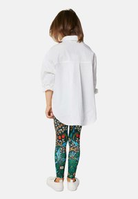 Fehér gombos ing, oversized szabású, felgöngyölt ujjakkal; színes virágmintás leggings-szel párosítva. Lábbelik: fehér sportcipő.