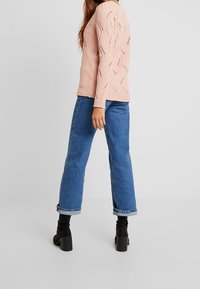 Lichtroze gebreide trui met een getextureerd, zigzagpatroon; gecombineerd met hooggesneden, ontspannen blauwe spijkerbroeken en zwarte enkellaarsjes met hak.