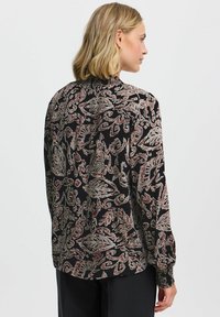 Blusa nera con un motivo floreale paisley in crema e bordeaux. Maniche lunghe con polsini arricciati, vestibilità aderente e scollatura rotonda.