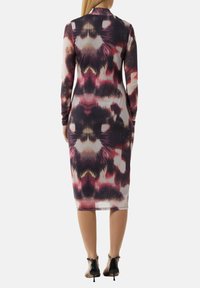 Langärmliges Kleid in einem mehrfarbigen abstrakten Muster mit taillierter Silhouette, knielangem Saum und weichem Stoff; kombiniert mit schwarzen High Heels.