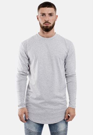 Langärmliges graues T-Shirt aus weichem Stoff mit einem Rundhalsausschnitt, das einen leicht abgerundeten Saum und angepasste Ärmel hat. Kombiniert mit gemusterten Jeans.