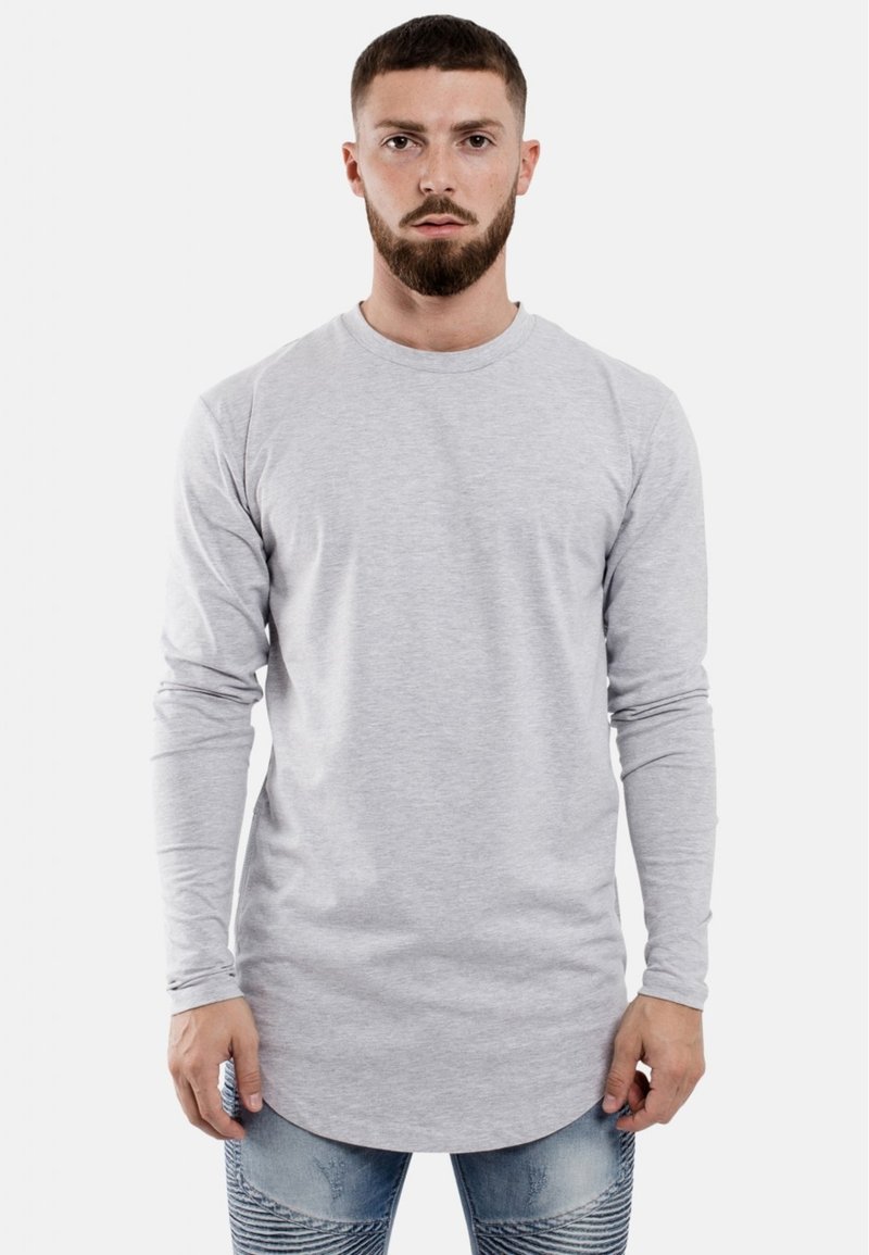 Langärmliges graues T-Shirt aus weichem Stoff mit einem Rundhalsausschnitt, das einen leicht abgerundeten Saum und angepasste Ärmel hat. Kombiniert mit gemusterten Jeans.