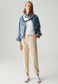Jeansjacke, weißes T-Shirt, beiger Chino und weiße Sneaker. Der Schal hat schwarze Streifen auf weißem Hintergrund. Lässiges Outfit mit hochgerollten Ärmeln.