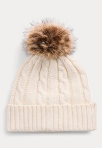 Zsinórmintás krémszínű sapka texturált bordázott mandzsettával és nagy, bolyhos barna pomponnal a tetején. Puha anyagból készült, melegen tartó dizájn.